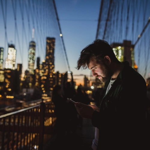 Man looking at mobile phone at Brooklyn Bridge at night.
